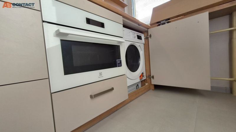Built-in washing machine and oven in the kitchen unit of a studio apartment with light flooring.