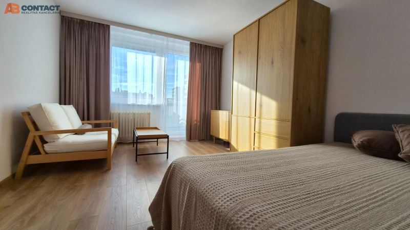 A room with a large window, a couch, a bed, a wardrobe, and a floor with a wooden decor in a studio apartment.