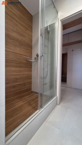 Shower corner with wooden decor in a studio apartment with white tiles.