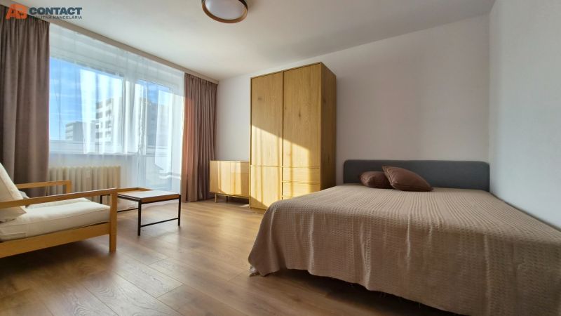 A bright room with a bed, chair, and furniture in a studio apartment, floor with wooden decor.