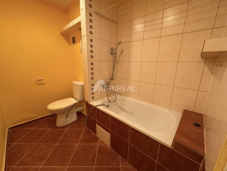 Bathroom in a one-room apartment with a bathtub and toilet with tiles in brown tones.