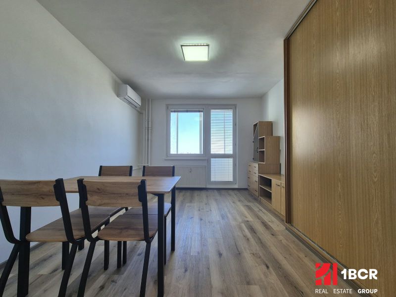 A studio apartment with a wooden floor, a table, chairs, and built-in wardrobes.