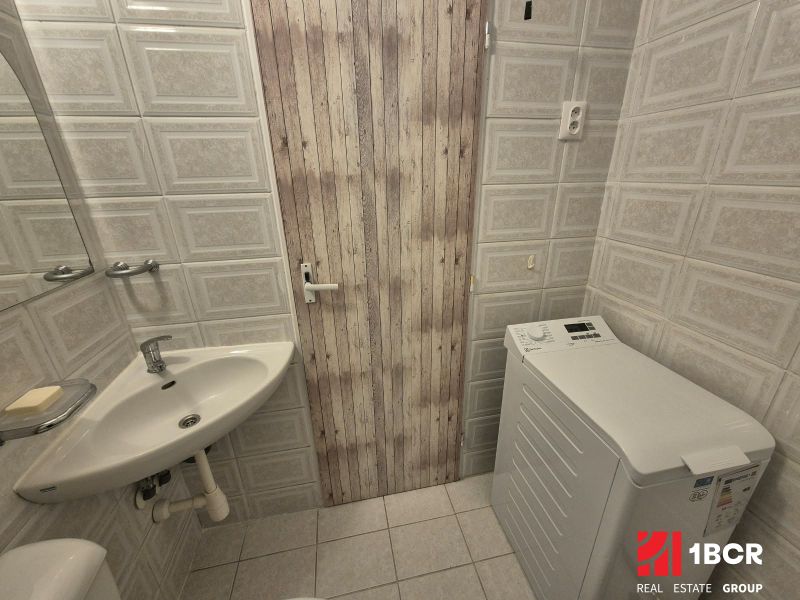 A studio apartment bathroom with a sink, washing machine, and ceramic tile cladding.