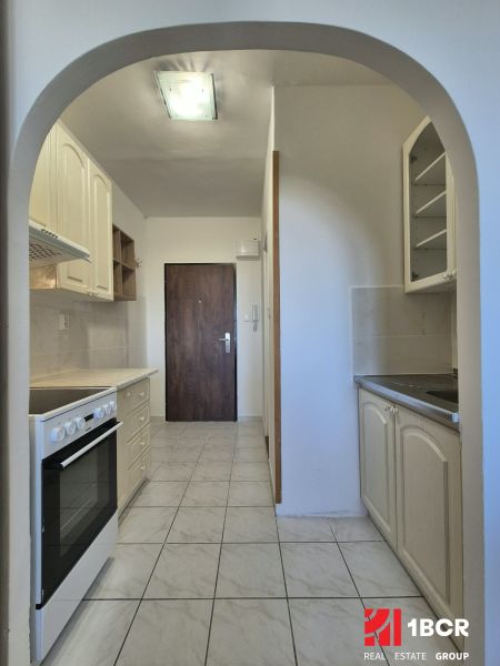 A kitchen in a studio apartment with white cabinets and white tiles on the floor.
