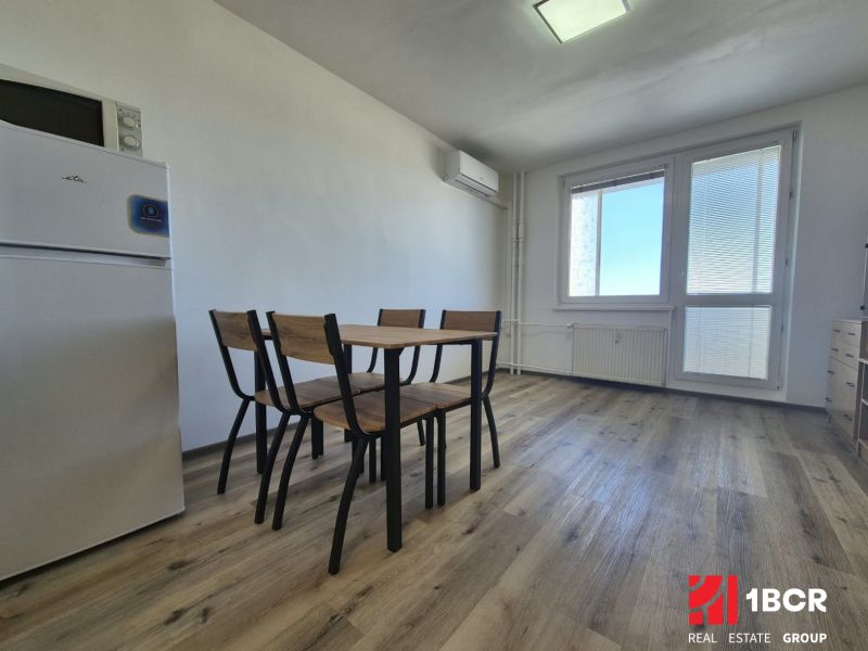Studio apartment with a refrigerator, wooden decor on the floor, and a dining table with chairs.