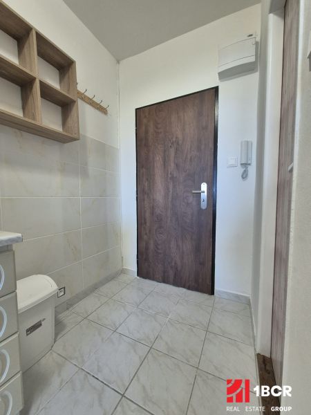 Studio apartment with a tiled floor, wooden shelf, and door with a wooden decor.
