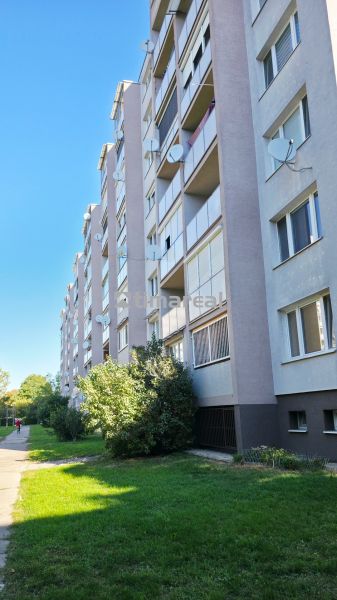 The exterior of a panel building in Trnava with greenery and a walkway to a 3-room apartment.