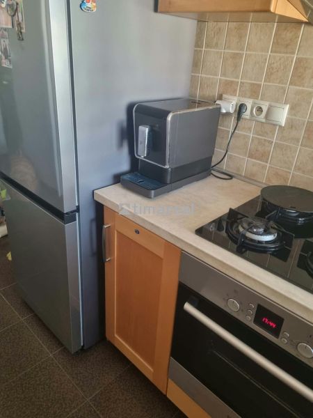 A kitchen in a 3-room apartment with a refrigerator, stove, and coffee maker on a stone countertop.