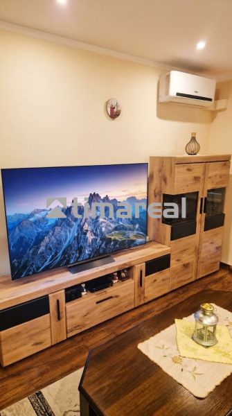 A living room with a television, decorative furniture, and a wooden-patterned floor in a three-room apartment.