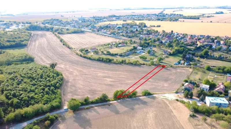 Agricultural and forest lands in Podhájska, surrounding fields and distant buildings.
