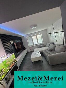 Living room of a two-room apartment with a wooden decor floor, a sofa, and an aquarium.