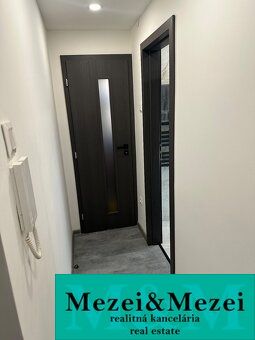 A hallway in a 2-room apartment with dark doors and a wall intercom.