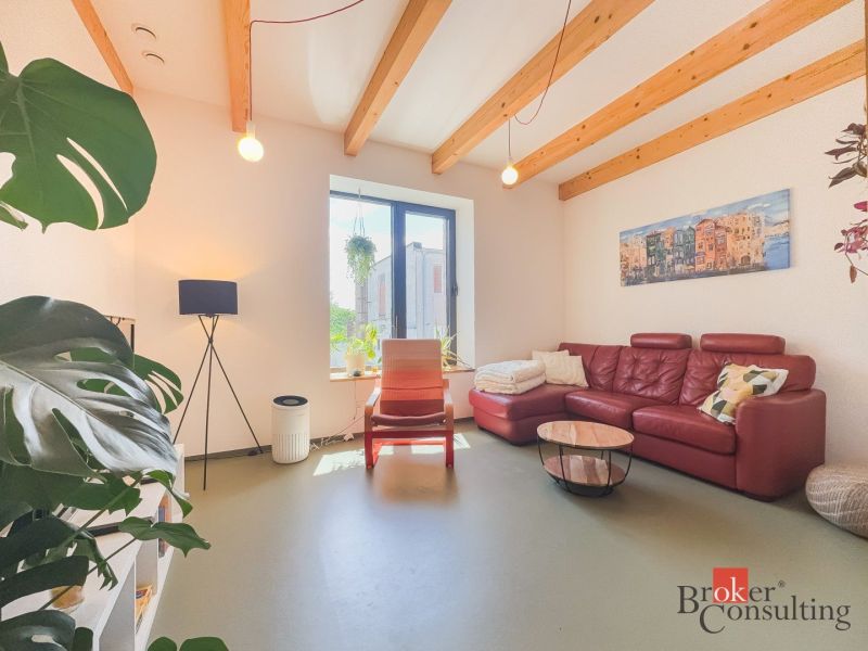 Living room in a 3-room apartment with a red sofa, plants, and wooden beams on the ceiling.
