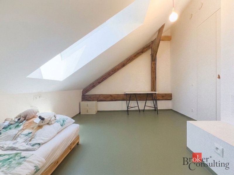 Attic room with a bed, wood-patterned floor, and a skylight in a 3-room apartment.