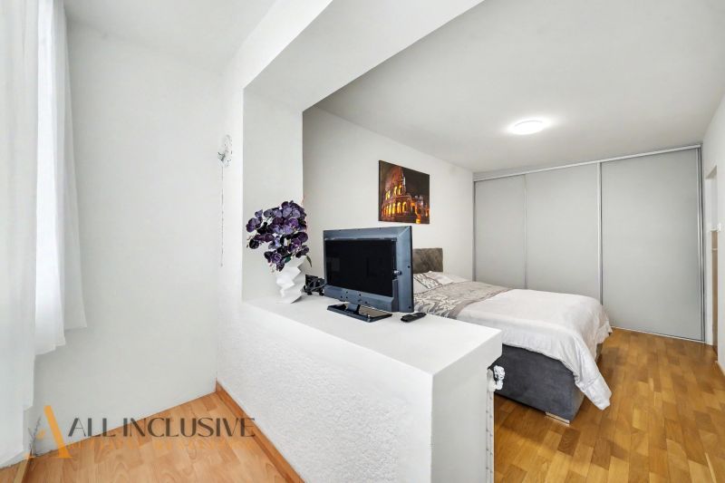 A bright bedroom with a TV, bed, and wood-decor flooring in a family house.
