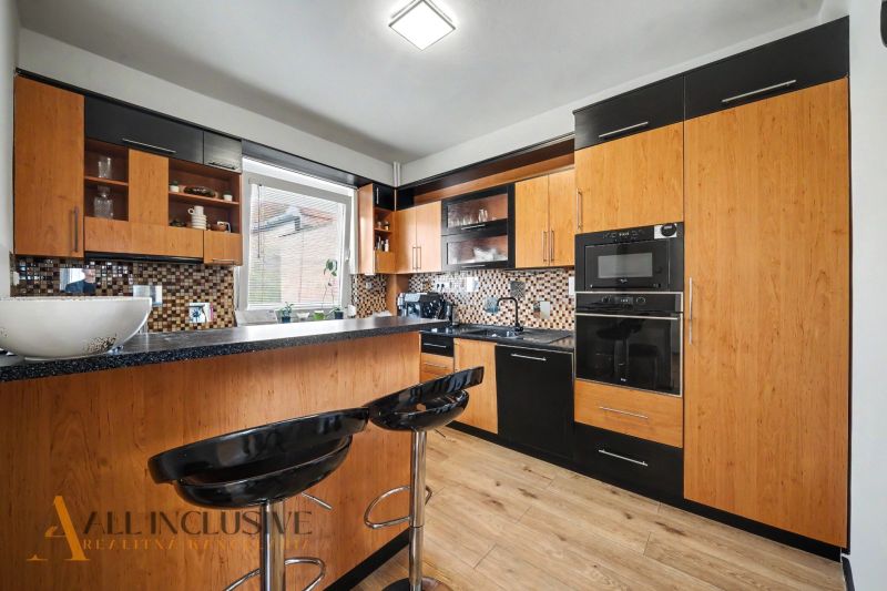 A kitchen with black furniture and a wood-patterned floor in a family house.