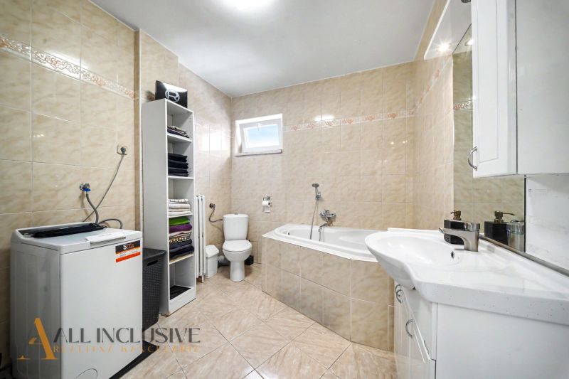 A bathroom in a family house with a bathtub, sink, washing machine, and shelving cabinet.
