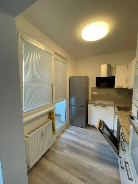 A kitchen in a 2-room apartment with a wooden decor floor, white cabinets, and a built-in appliance.