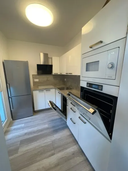 A kitchen with a built-in oven, white cabinets, and a wood-patterned floor in a 2-room apartment.