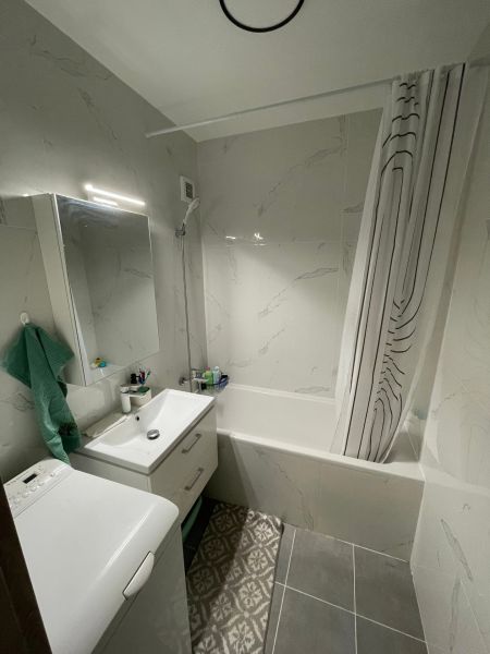 Bathroom in a 2-room apartment with a bathtub, sink, washing machine, and tiles.