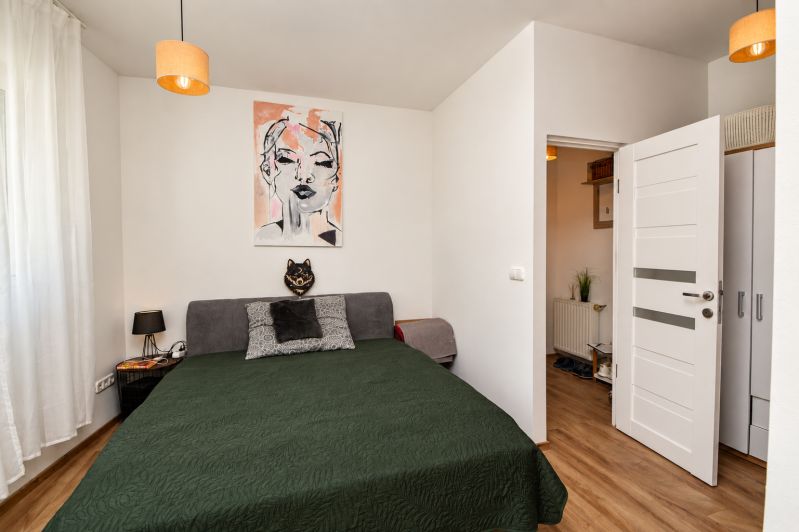 A bedroom in a studio apartment with a painting, a gray couch, and a wooden decor floor.