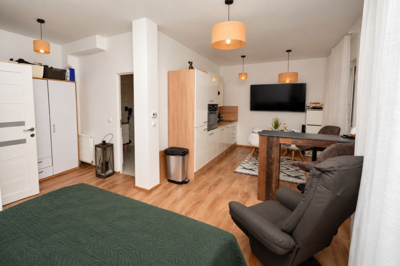 A one-room apartment with a wooden decor floor, a kitchen unit, and a dining area.