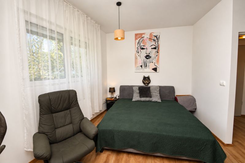 A bedroom in a studio apartment with an armchair, a bed, and a wood-decor floor.