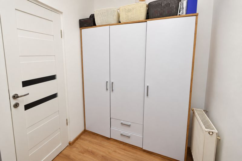 White cabinet with baskets, doors, and floor with wood decor in a studio apartment.