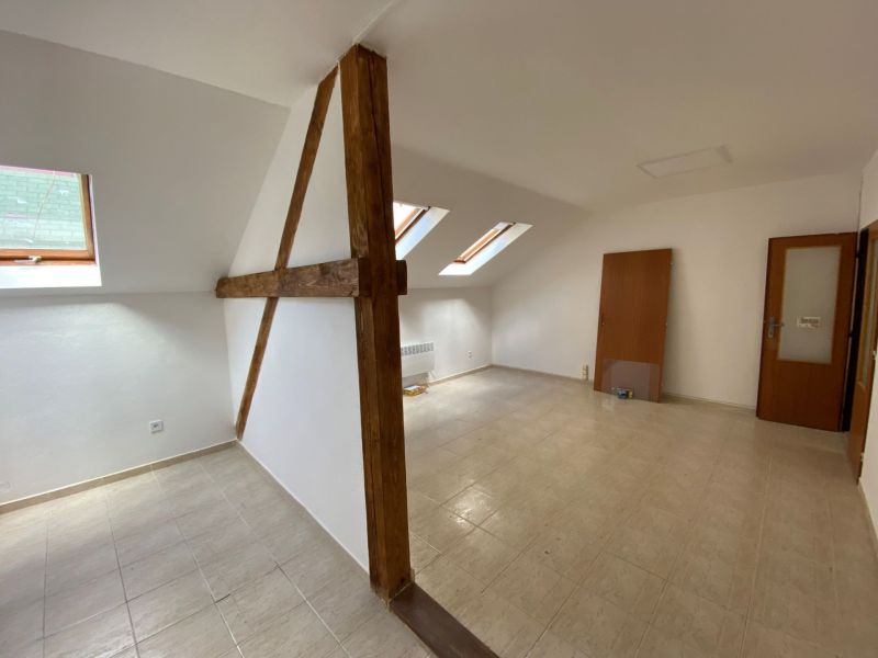 An attic office with wooden beams and slanted windows, floor with wooden decor.