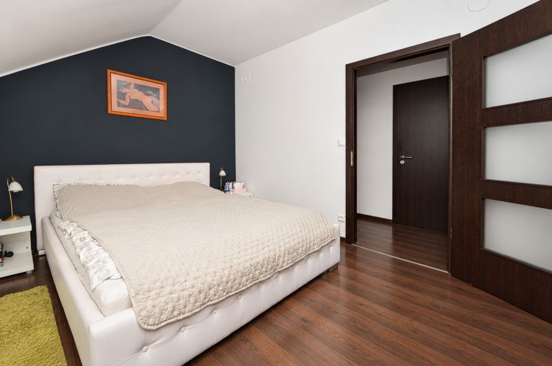 Bright bedroom with a bed and wood-patterned floor in a family house.