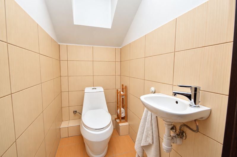 A bathroom in a family house with a toilet and a sink, beige tiles.