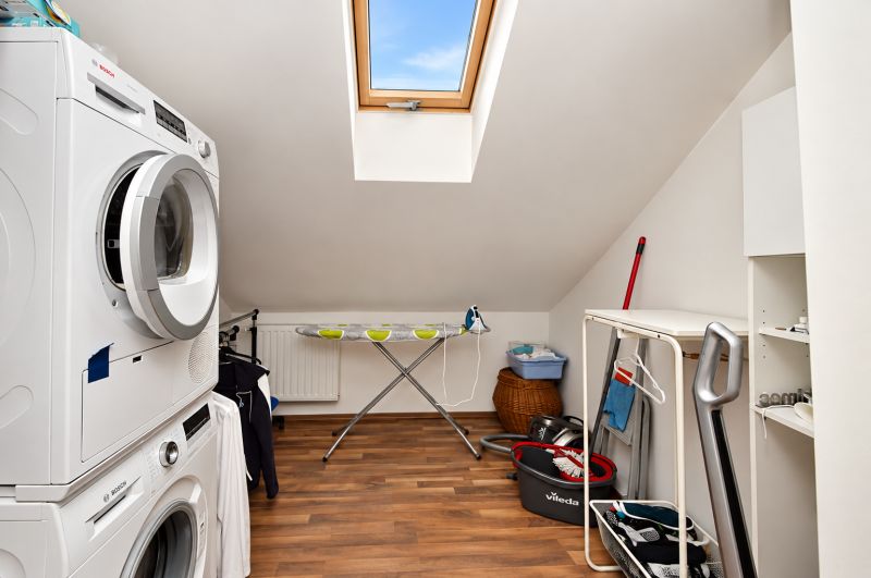 Laundry room in the attic of a family house with a wooden decor floor.