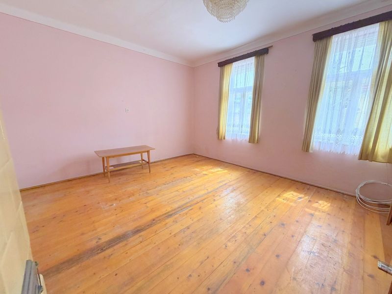 A room in a family house with a wooden decor floor, a table, and curtains.