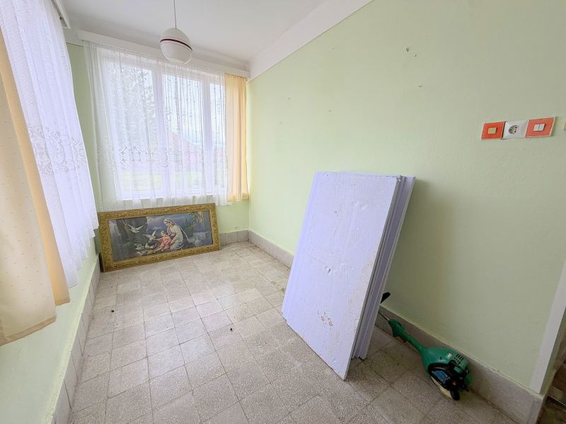 The interior of a family house with a painting, windows with white curtains, and green walls.