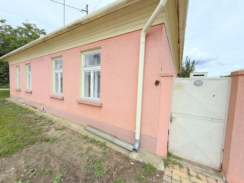 A family house in Dunakiliti with a pink facade, white windows, and a gate.