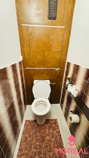 A toilet in a 3-room apartment with brown tiles and a mat.