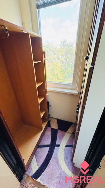 A wardrobe in a 3-room apartment with a view through a large window and a colorful carpet.