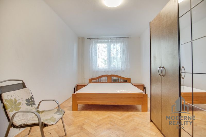 Bedroom in a 2-room apartment with a double bed, chair, and wooden decor flooring.