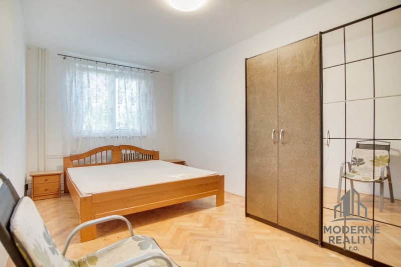 A bedroom in a 2-room apartment with a wood-patterned floor, a bed, and a wardrobe.