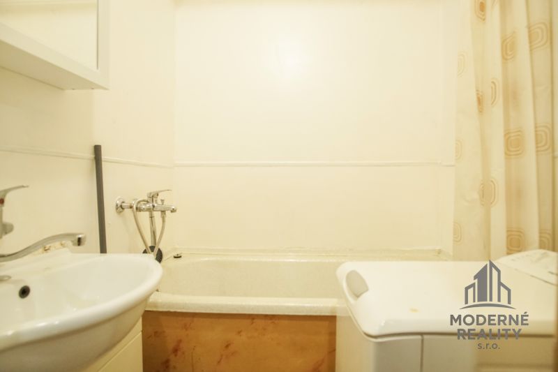 A bathroom in a two-room apartment with a sink, bathtub, and washing machine.