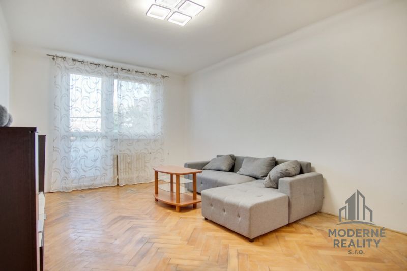Living room in a two-room apartment with a wooden decor floor and a gray sofa.