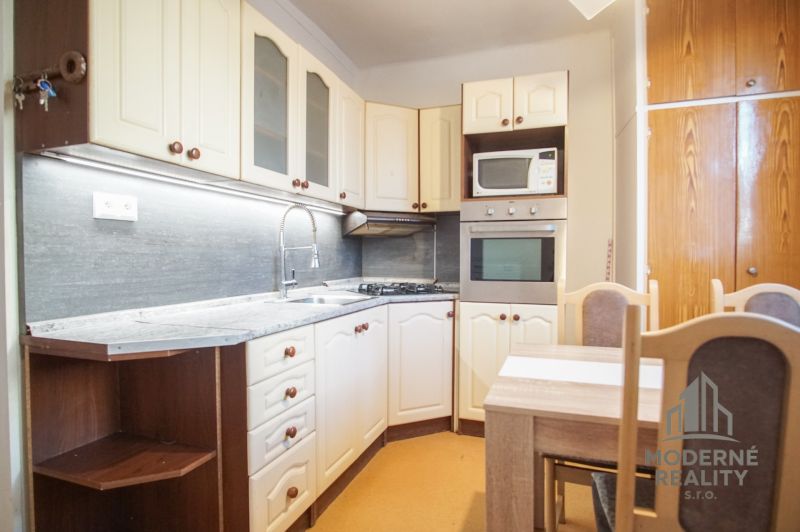 A kitchen in a 2-room apartment with white cabinets and a dining table.