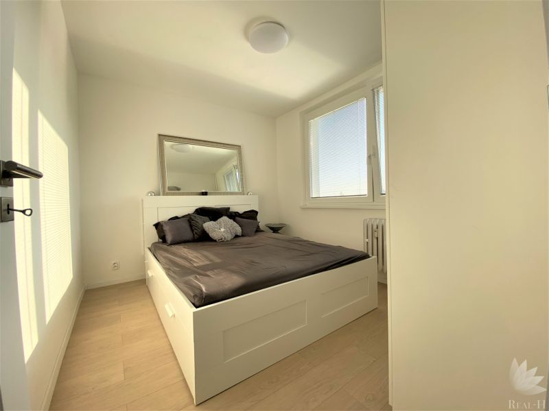 A bedroom with a large bed, a mirror, and windows in a 3-room apartment.