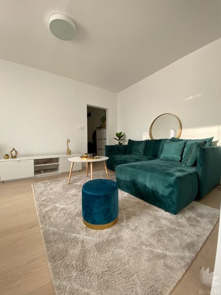 Living room in a three-room apartment with a dark green sofa and a table on a light carpet.