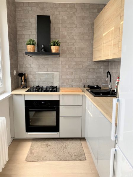 Compact kitchen in a 3-room apartment with a stove, sink, and gray brick tiles.