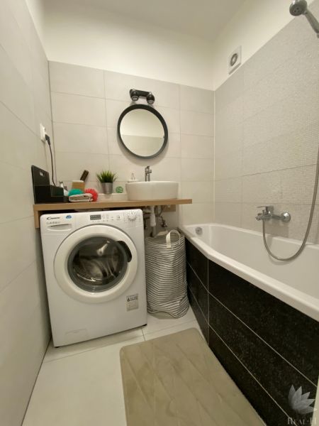 Bathroom of a 3-room apartment with a washing machine, bathtub, sink, and round mirror.