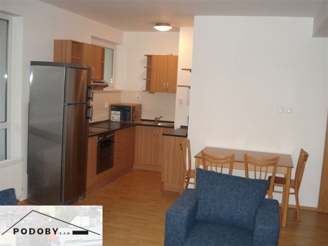 A kitchen in a 3-room apartment with a kitchen unit, dining table, and a floor with a wood decor.