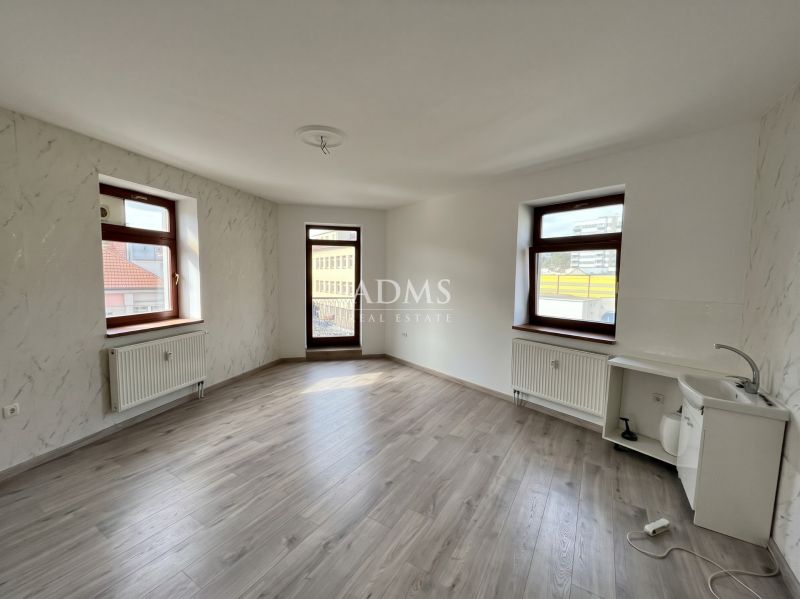 A room with windows, white walls, a wood-patterned floor, and a sink in the office.