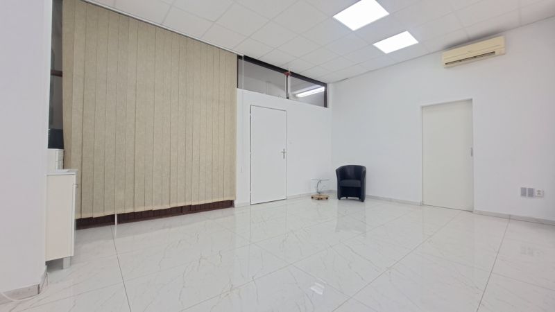 A white room with a ceramic floor, an armchair, a table, and vertical blinds.