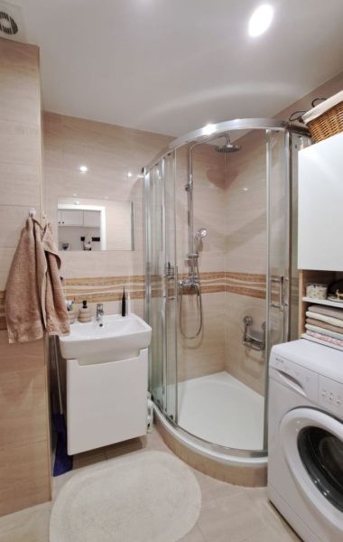 Bathroom with a sink, shower, and washing machine in a 3-room apartment, beige tiles.